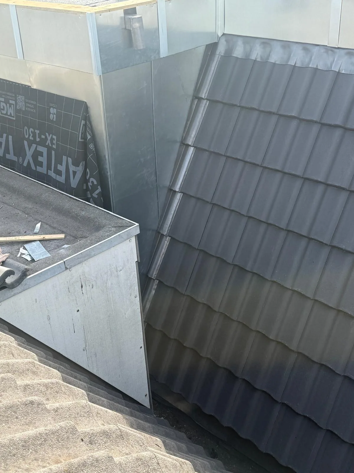 Metalen bekleding van een dakopbouw naast een donker pannendak.
